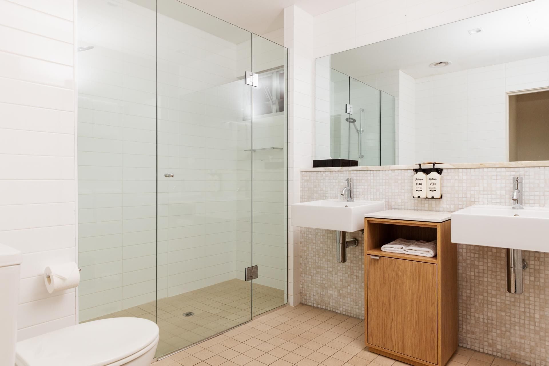A modern bathroom with a glass-enclosed shower, two sinks, a mirror, and a wooden cabinet.