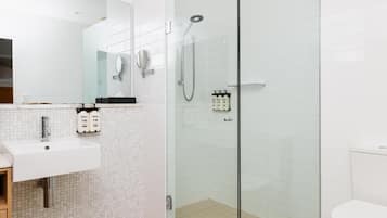 Un baño moderno con ducha acristalada, lavabo con espejo y artículos de aseo.