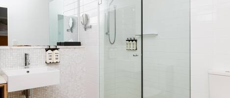A modern bathroom with a glass-enclosed shower, a sink with a mirror, and toiletries.