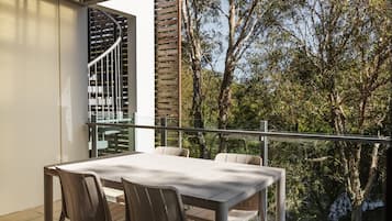 Un balcon avec une table et des chaises, un escalier en colimaçon et une vue sur les arbres.
