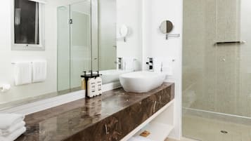 A modern bathroom with a large mirror, two sinks, a glass shower enclosure, and marble countertops.