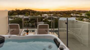 A hot tub with two chairs and a bottle of champagne, overlooking a residential area during sunset.