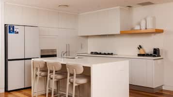 A modern kitchen with a central island, bar stools, a refrigerator, and a stove.