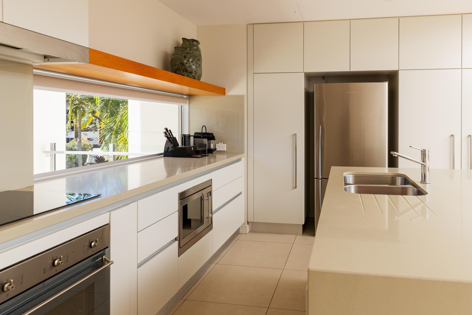 A modern kitchen with a stainless steel refrigerator, built-in oven, and a large window overlooking greenery.