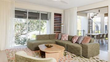 A modern living room with a sectional sofa, a coffee table, and a dining area with a spiral staircase.