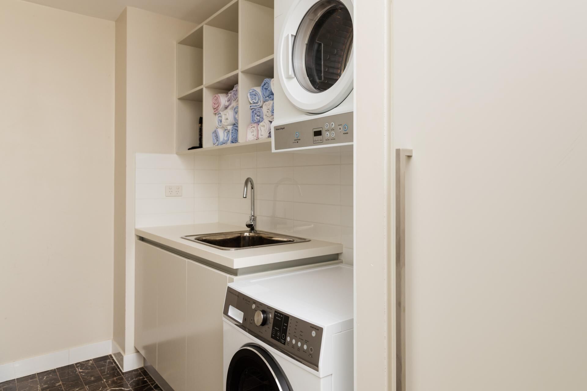 A laundry room with a washing machine, a sink, and a shelf with folded towels.