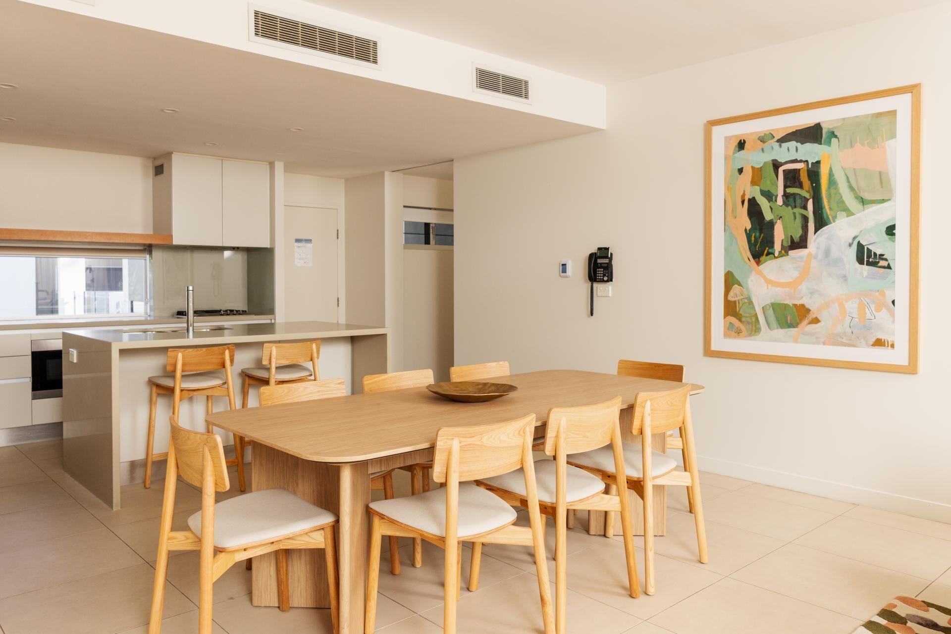 A modern kitchen with a dining area, a phone, and a painting on the wall.