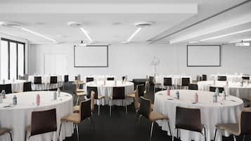 Une salle de conférence équipée de plusieurs tables rondes, chacune étant pourvue de chaises et de bouteilles d’eau.