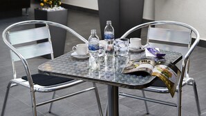 Una mesa con sillas, una revista y botellas de agua. Hay plantas en macetas y una pared con iluminación empotrada.