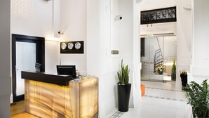Zona de recepción de hotel con un diseño moderno, que incluye un mostrador de recepción, relojes de pared y una planta en maceta.