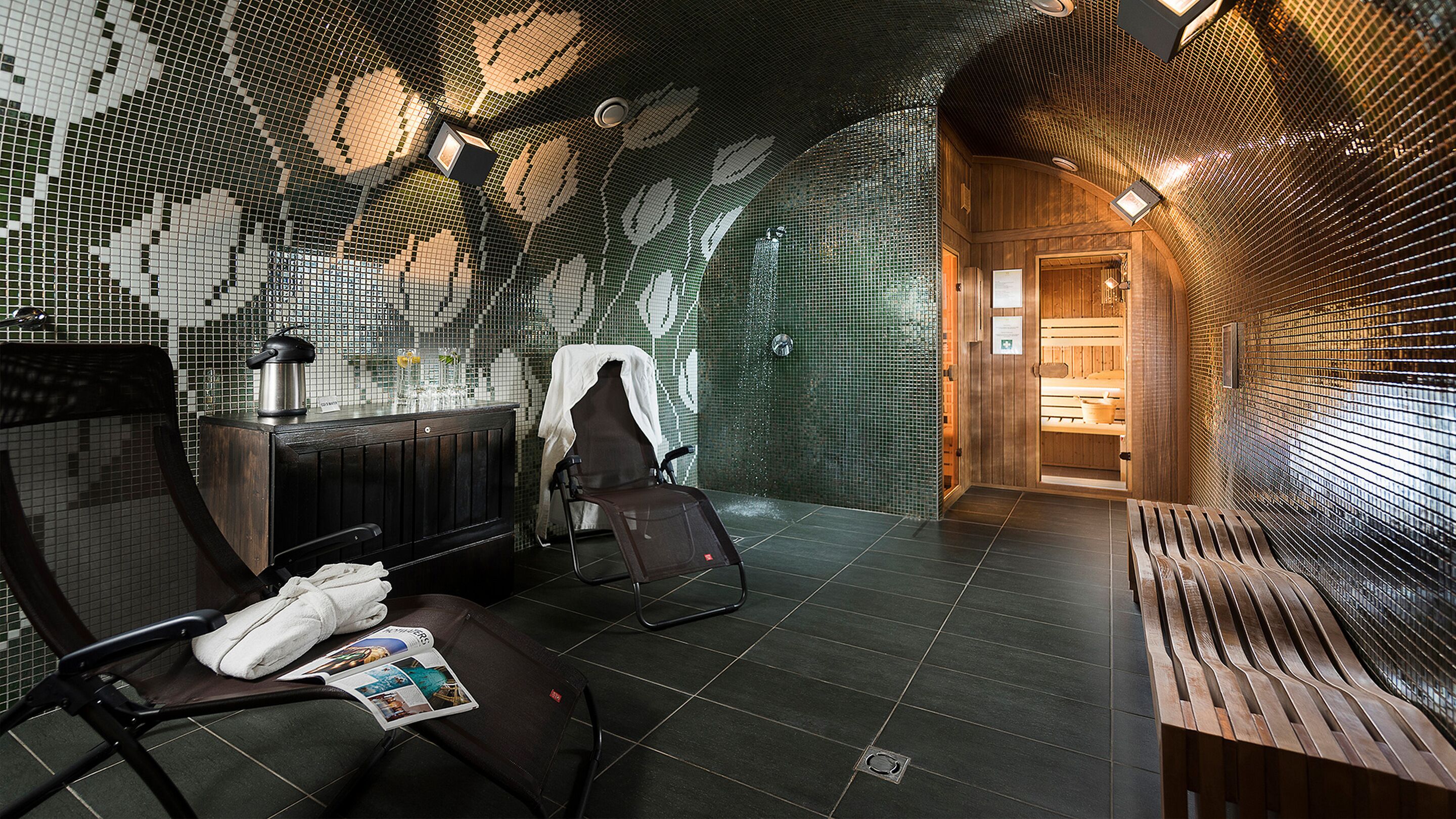 A spa room with a mosaic wall, a massage chair, a bench, and a small reading area with a magazine.