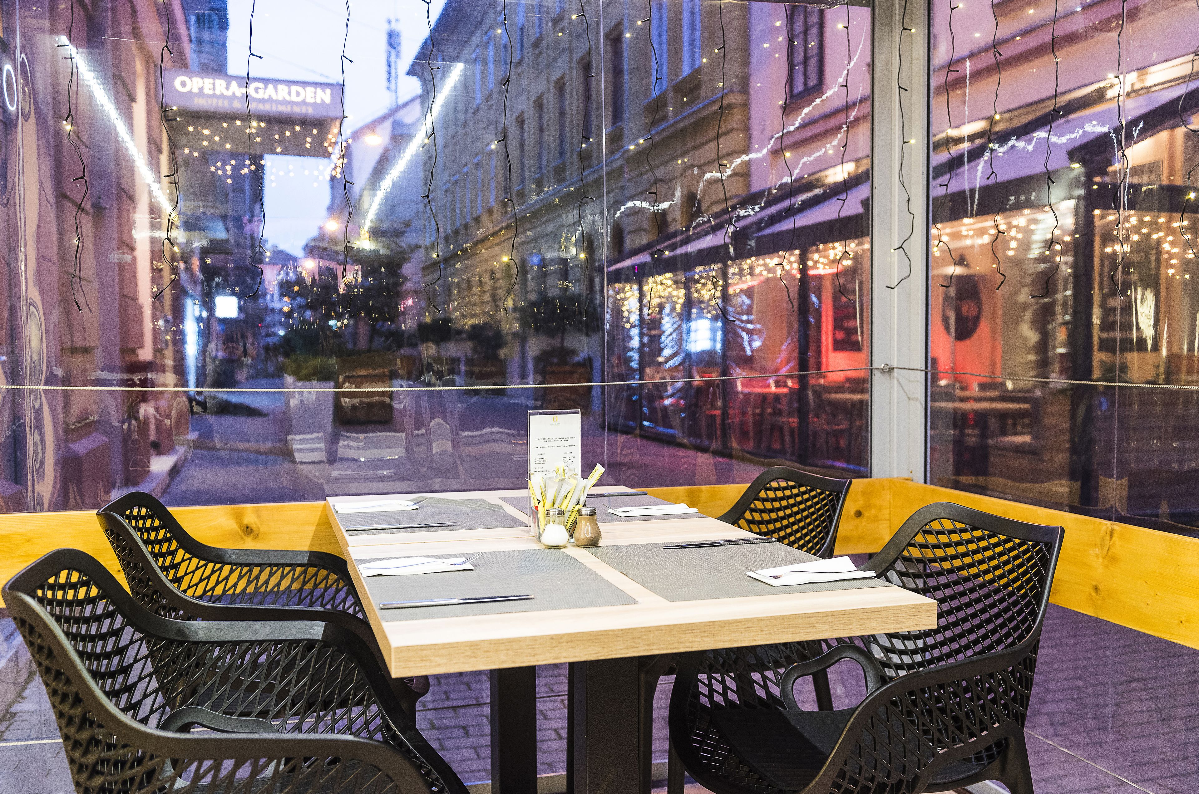 An outdoor dining area with a table set for two, chairs, and a menu stand.