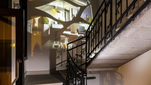 Una escalera con barandilla de metal, una puerta y una pared con ventana que proyecta sombras.