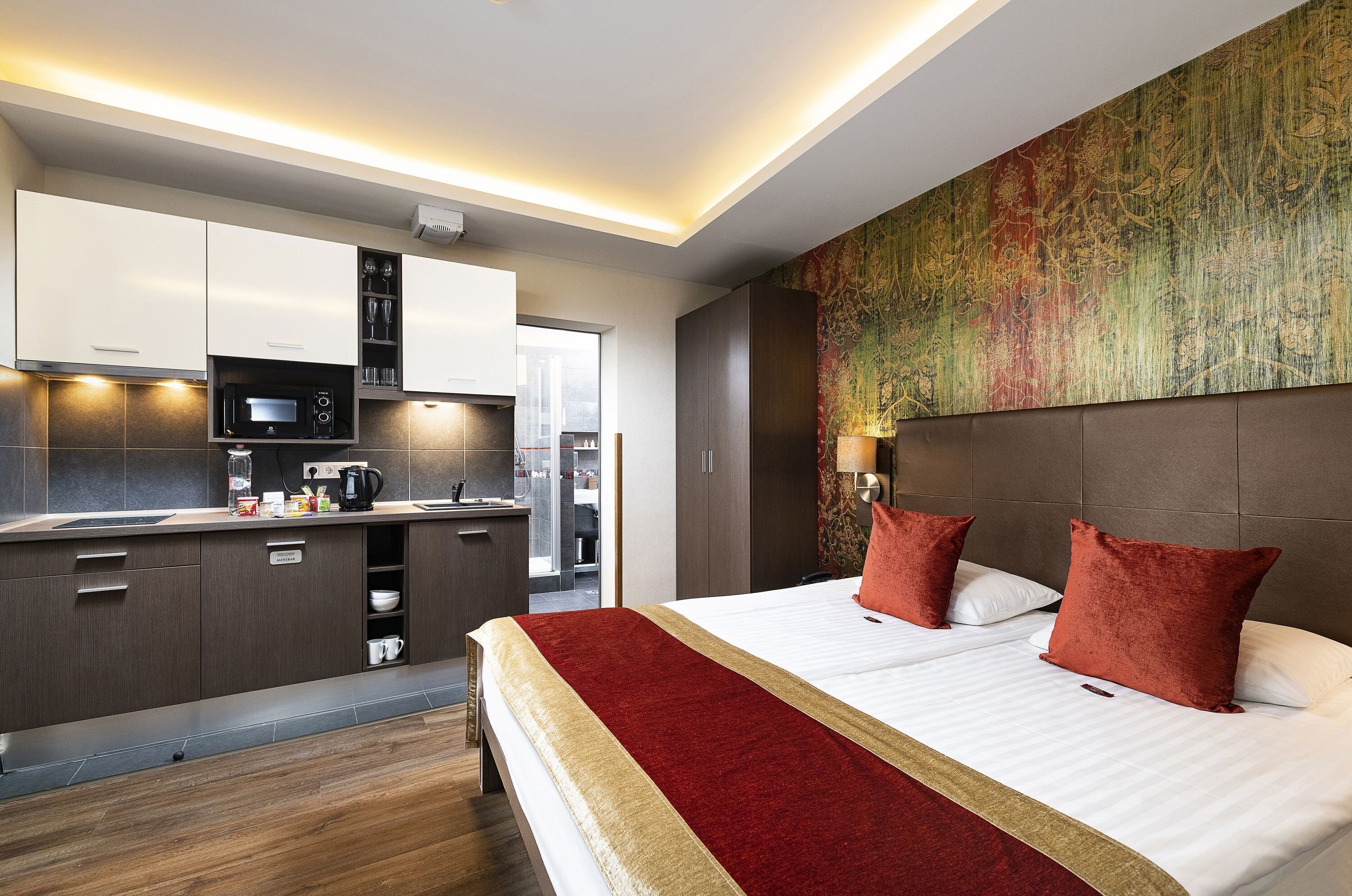 A modern hotel room with a large bed, a separate kitchenette, and a view of the city.