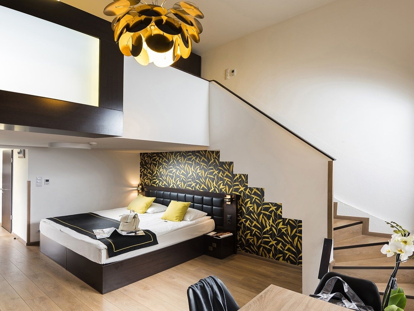 A modern bedroom with a bed, a staircase, and a unique ceiling light fixture.