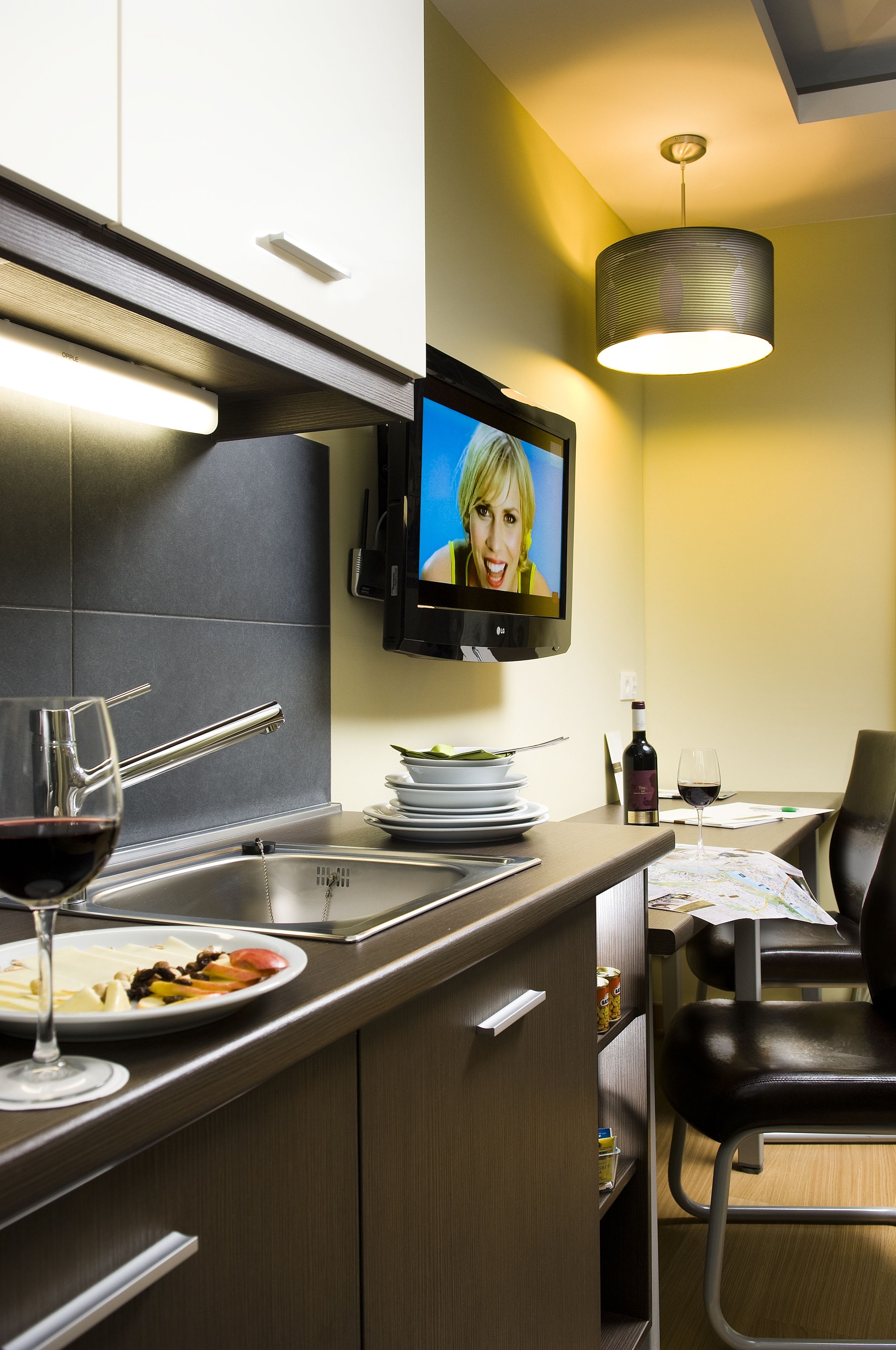 A modern kitchen with a flat-screen TV, wine glasses, and a dining area with a table and chairs.