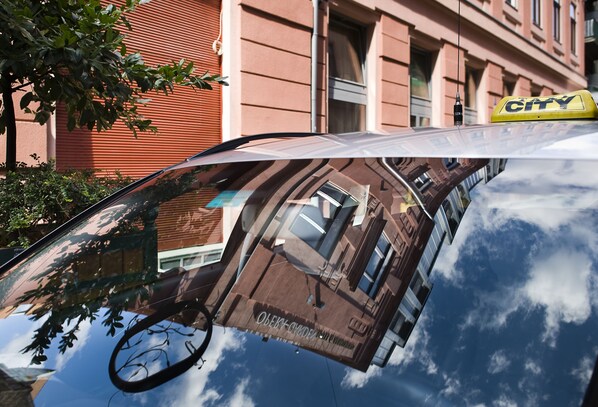 A car with a 'Taxi City' sign on the roof, reflecting a building with large windows and a red facade.