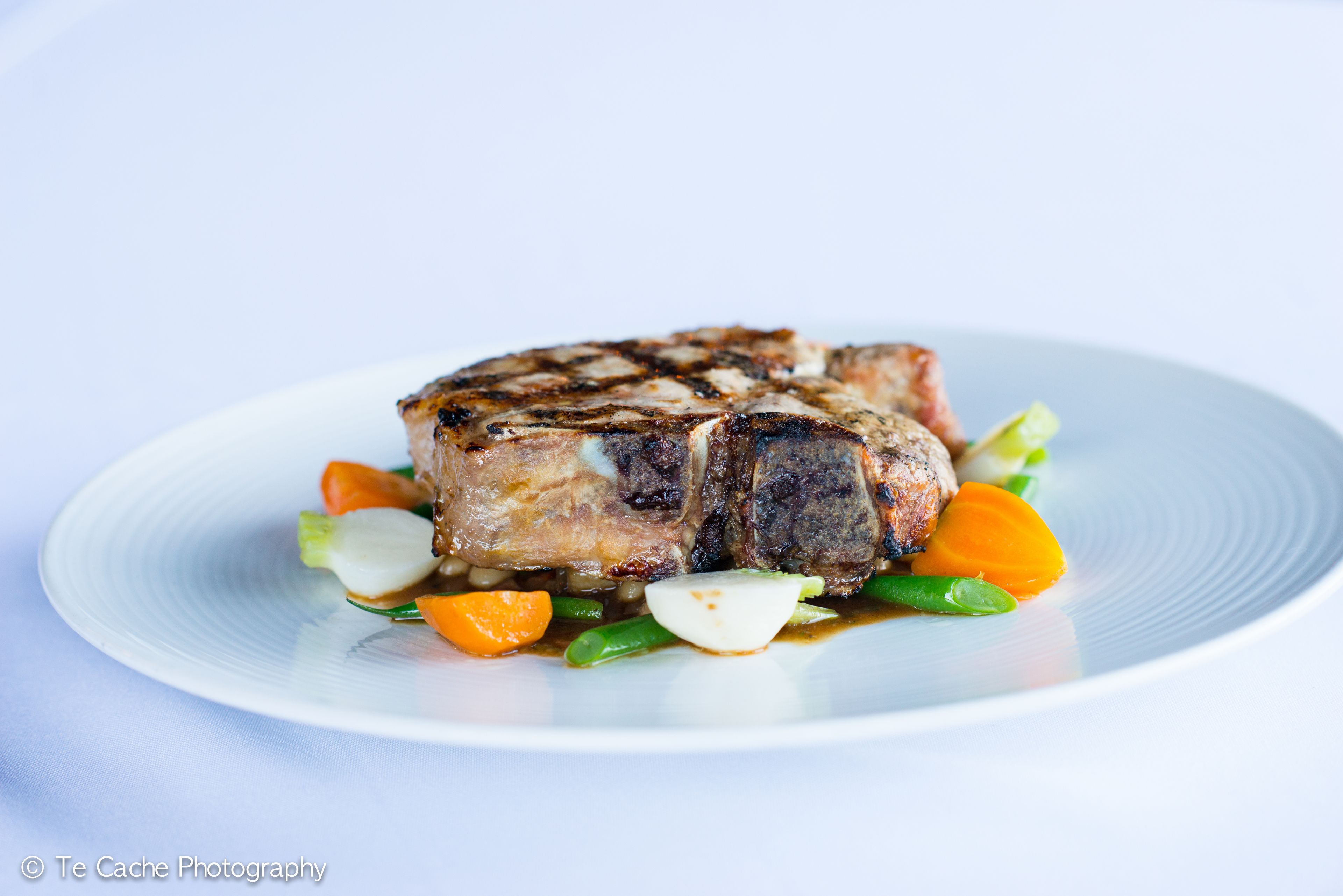 Egy tányér, rajta grillezett steak, zöldségek és mártás.