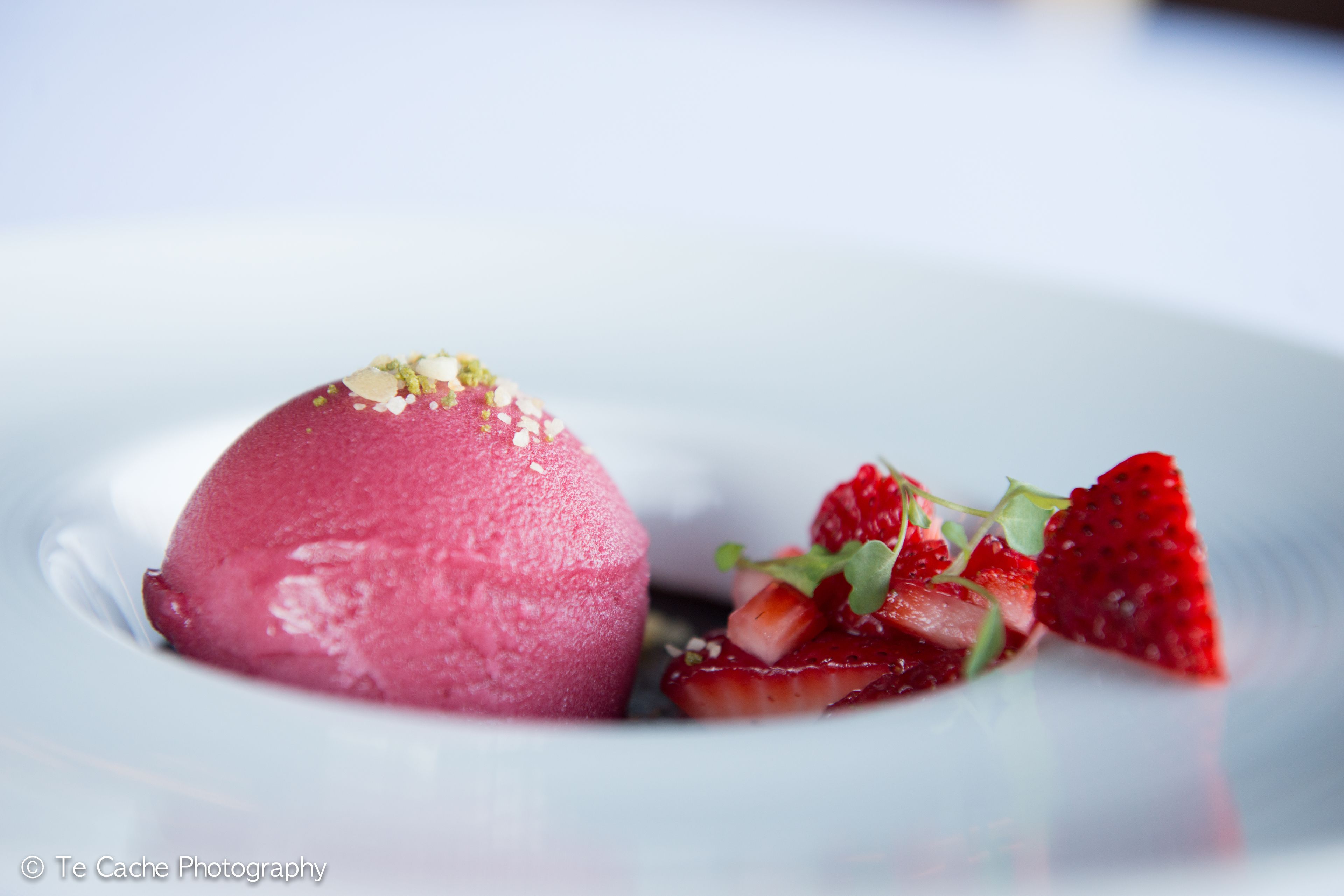 Un postre con una porción rosada y fresas sobre un plato blanco.