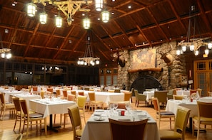 A spacious dining area with multiple tables and chairs, a stone wall with a mounted deer head, and a fireplace. - Overlook Lodge at Bear Mountain (Bear Mountain)
