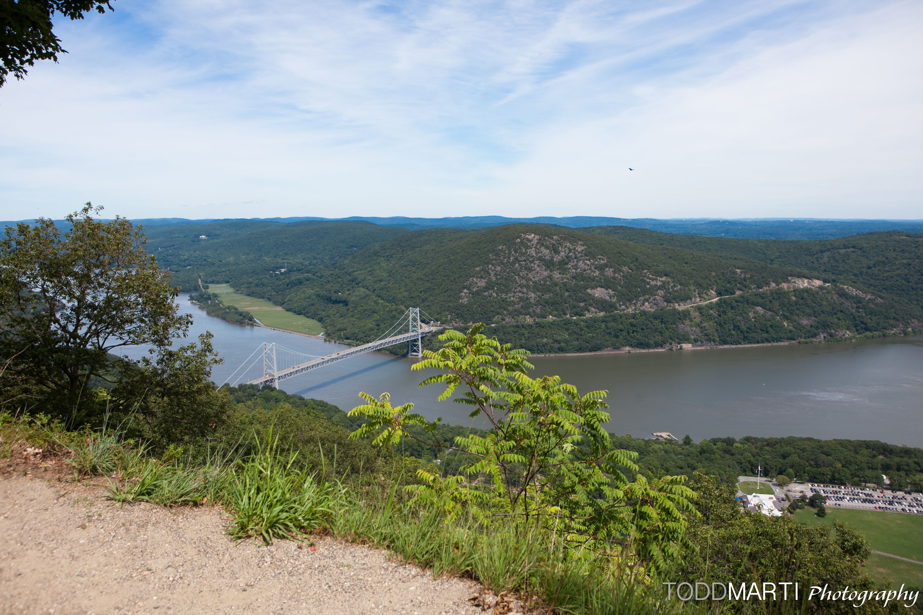 Una vista panorámica de un río con un puente, rodeado de abundante vegetación y colinas.