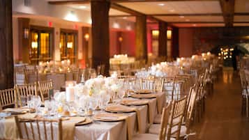 A long banquet hall with rows of tables set for a formal event, featuring candles and floral centerpieces.