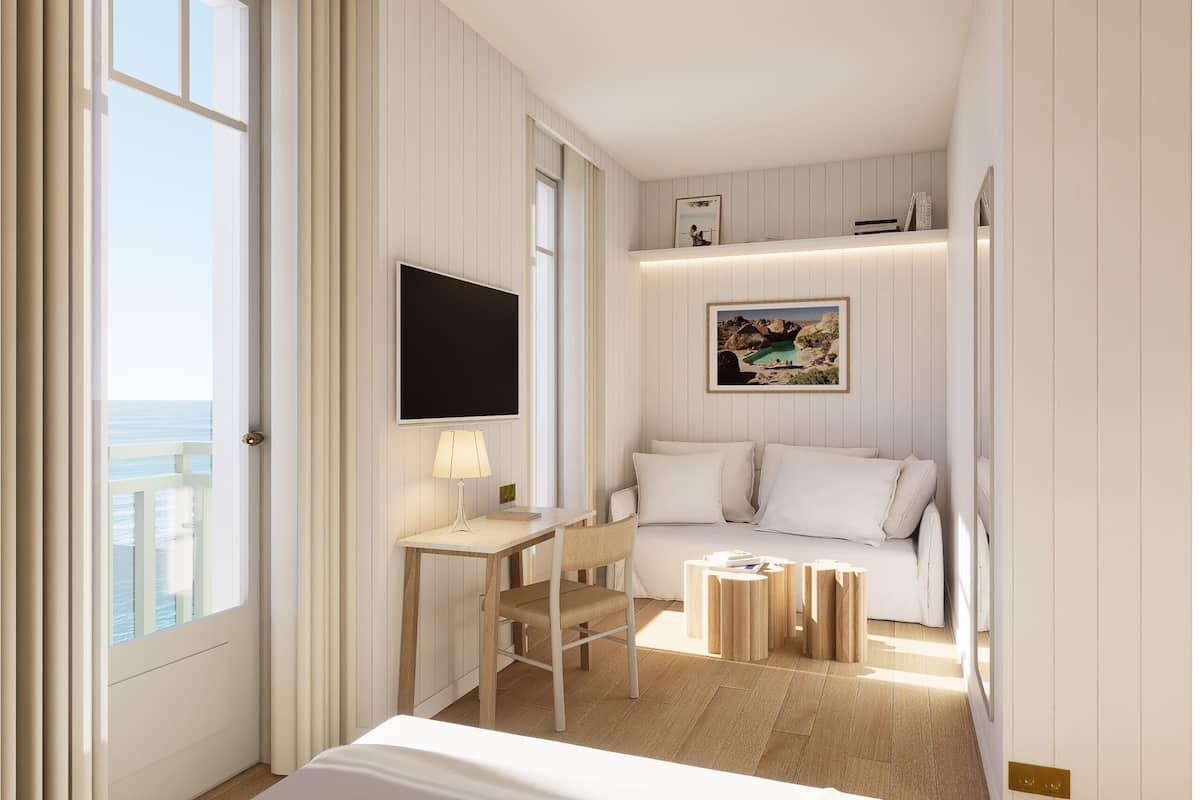 A hotel room with a bed, a desk, a chair, a TV, a sofa, and a small table.