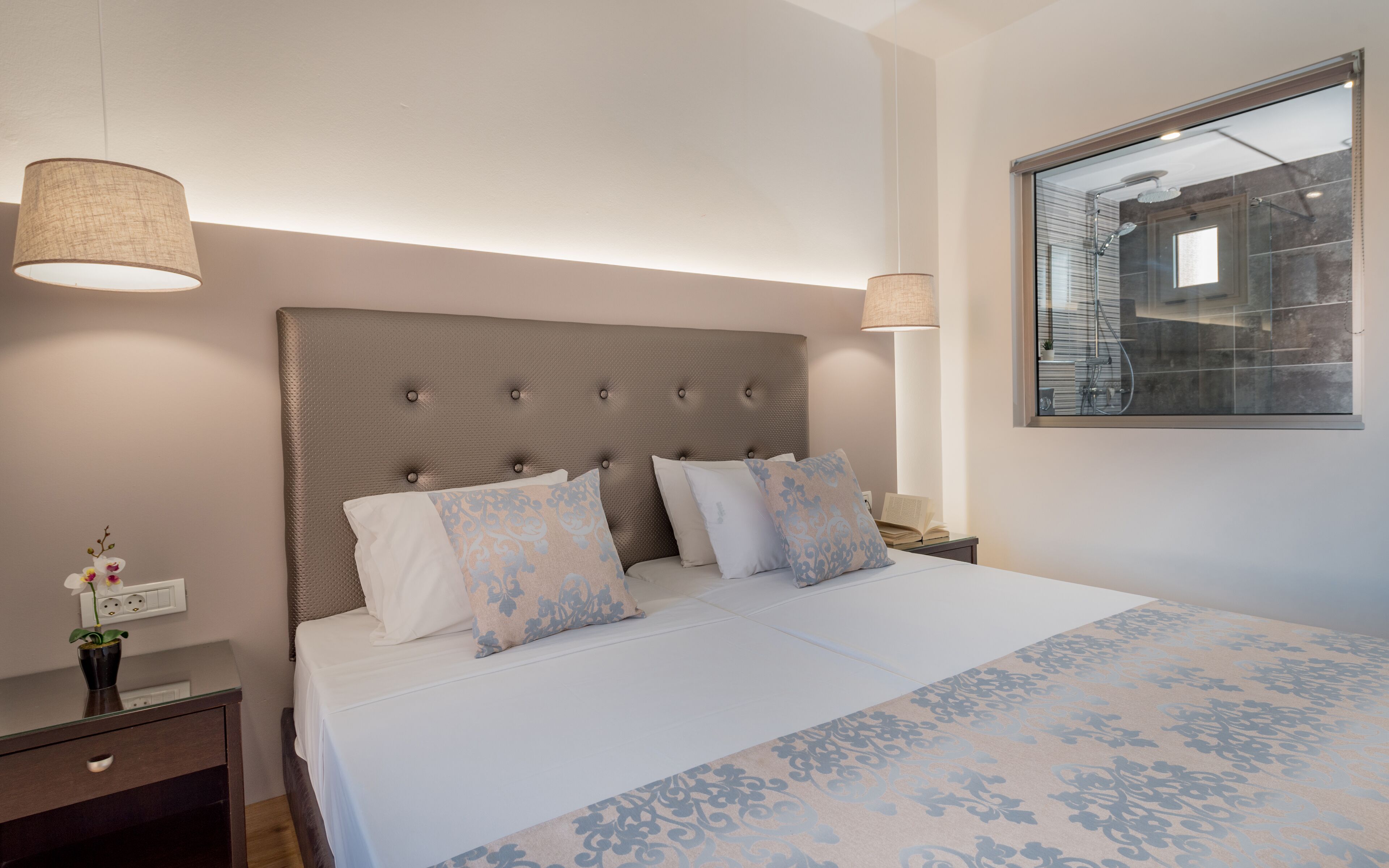 A neatly made bed with a patterned bedspread, a tufted headboard, and two bedside lamps.