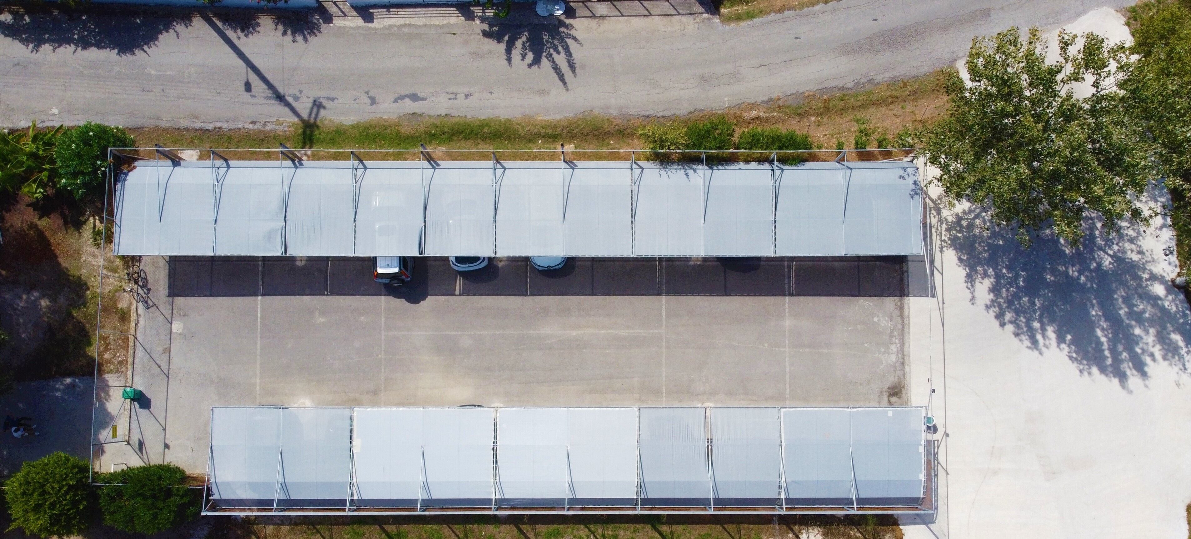 Vue aérienne d’un parking comportant plusieurs rangées de voitures garées et une grande zone couverte équipée de panneaux solaires.