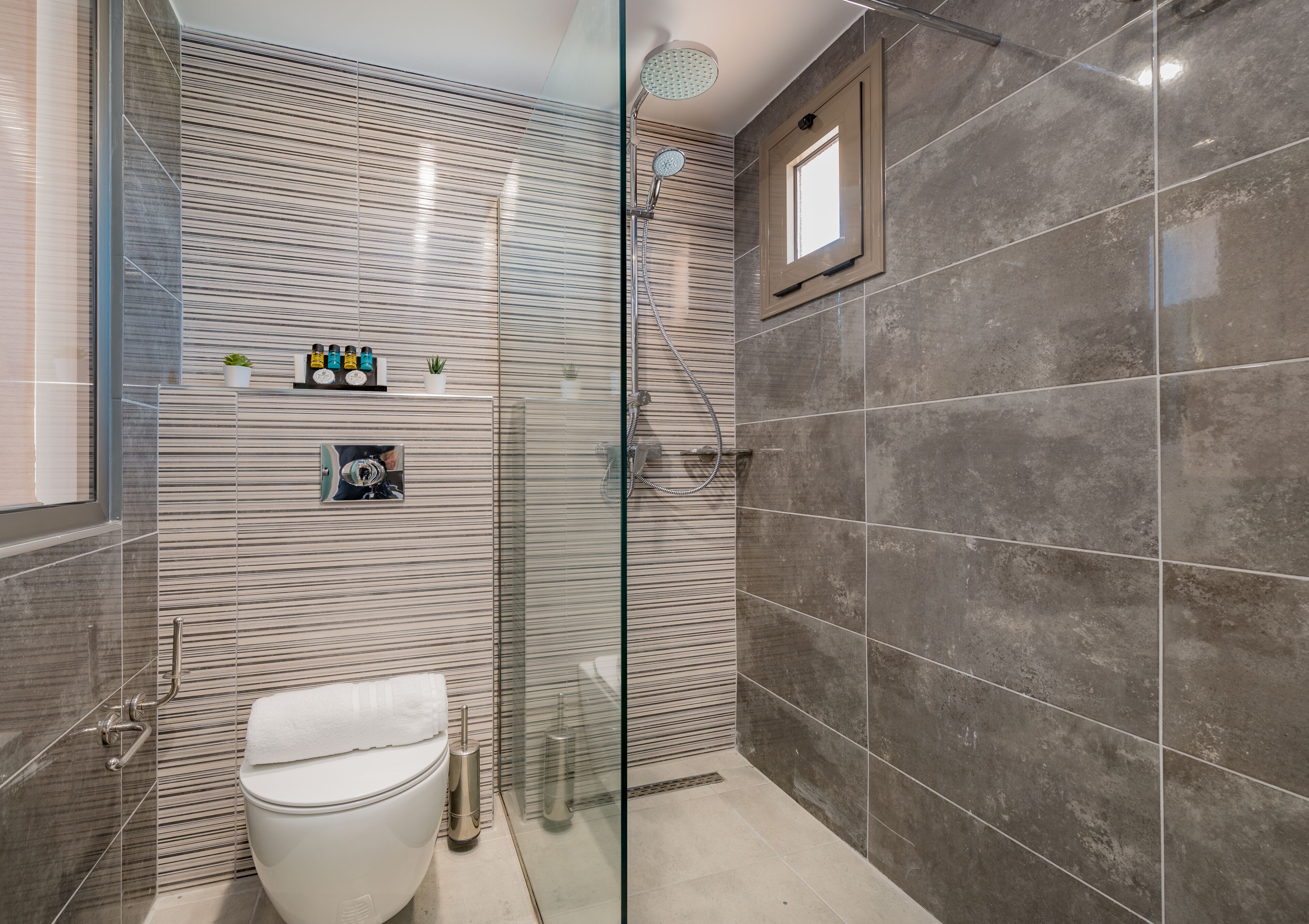 Ein modernes Badezimmer mit Duschkabine aus Glas, Toilette und kleinem Fenster.