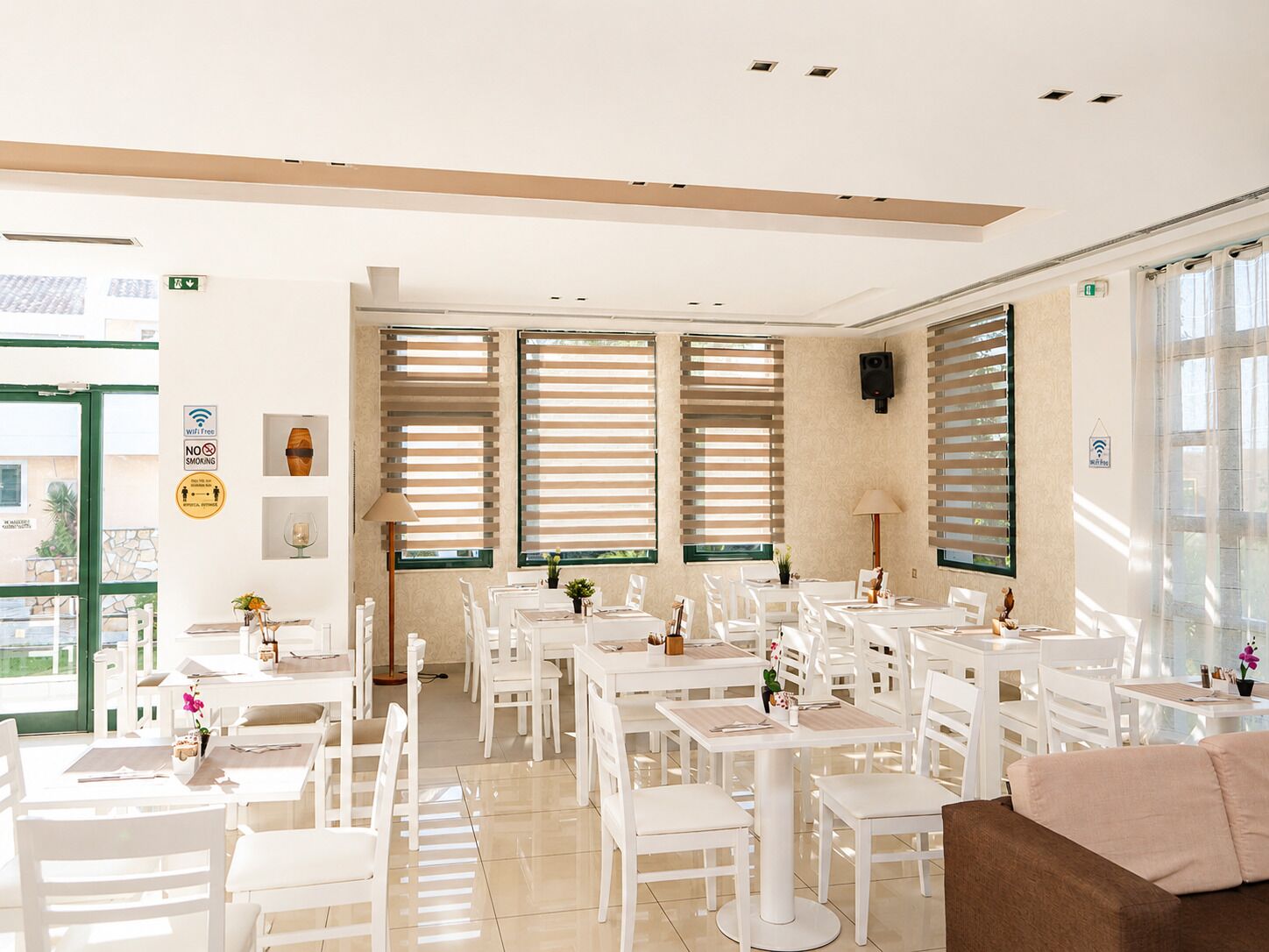 A spacious indoor area with multiple tables and chairs, large windows with blinds, and a green door.