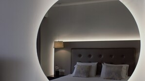 A modern bedroom with a circular mirror on the wall, a neatly made bed, a bedside table with a lamp, and a small potted plant. - Oscar Hotel (Zakynthos)