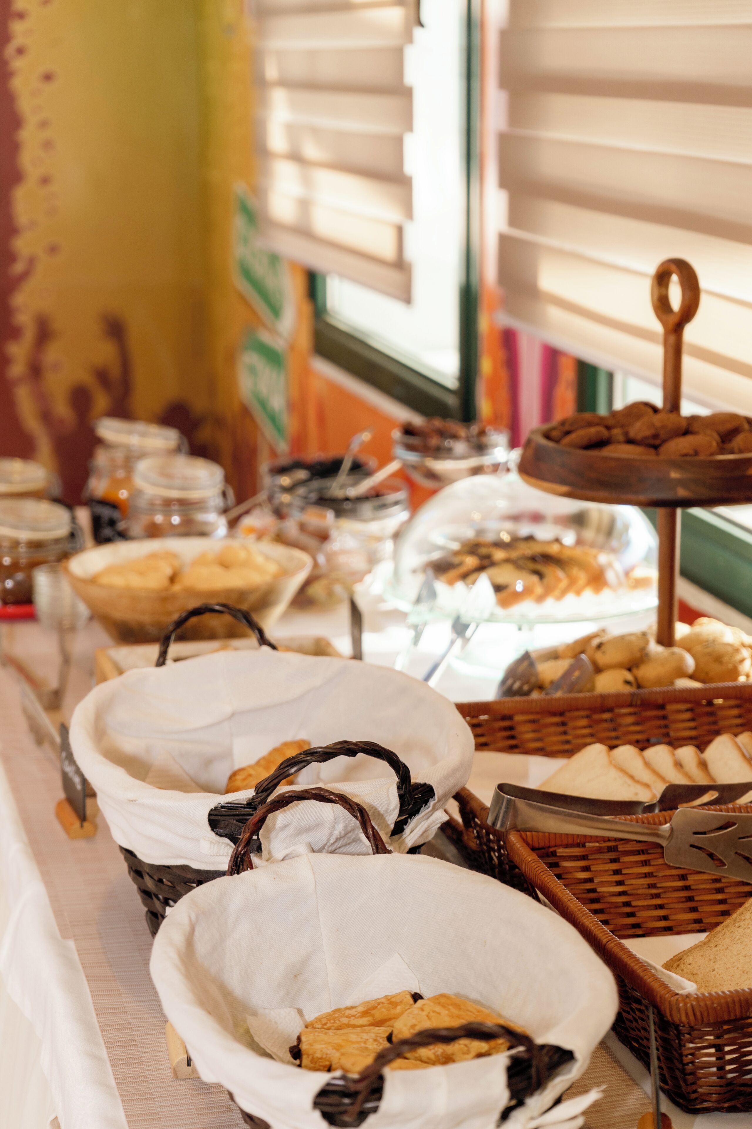 Een buffet met diverse soorten eten in manden en bakken, een raam met jaloezieën en een muur met een poster.