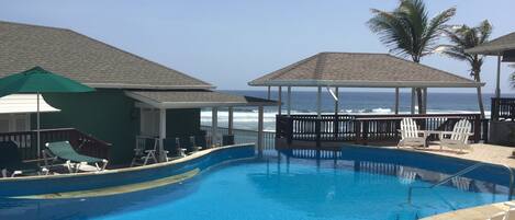 A swimming pool with lounge chairs and umbrellas, overlooking the ocean.