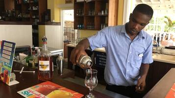 Um bartender preparando uma bebida num bar, com estantes cheias de garrafas e um aviso a indicar que o acesso é proibido aos hóspedes.