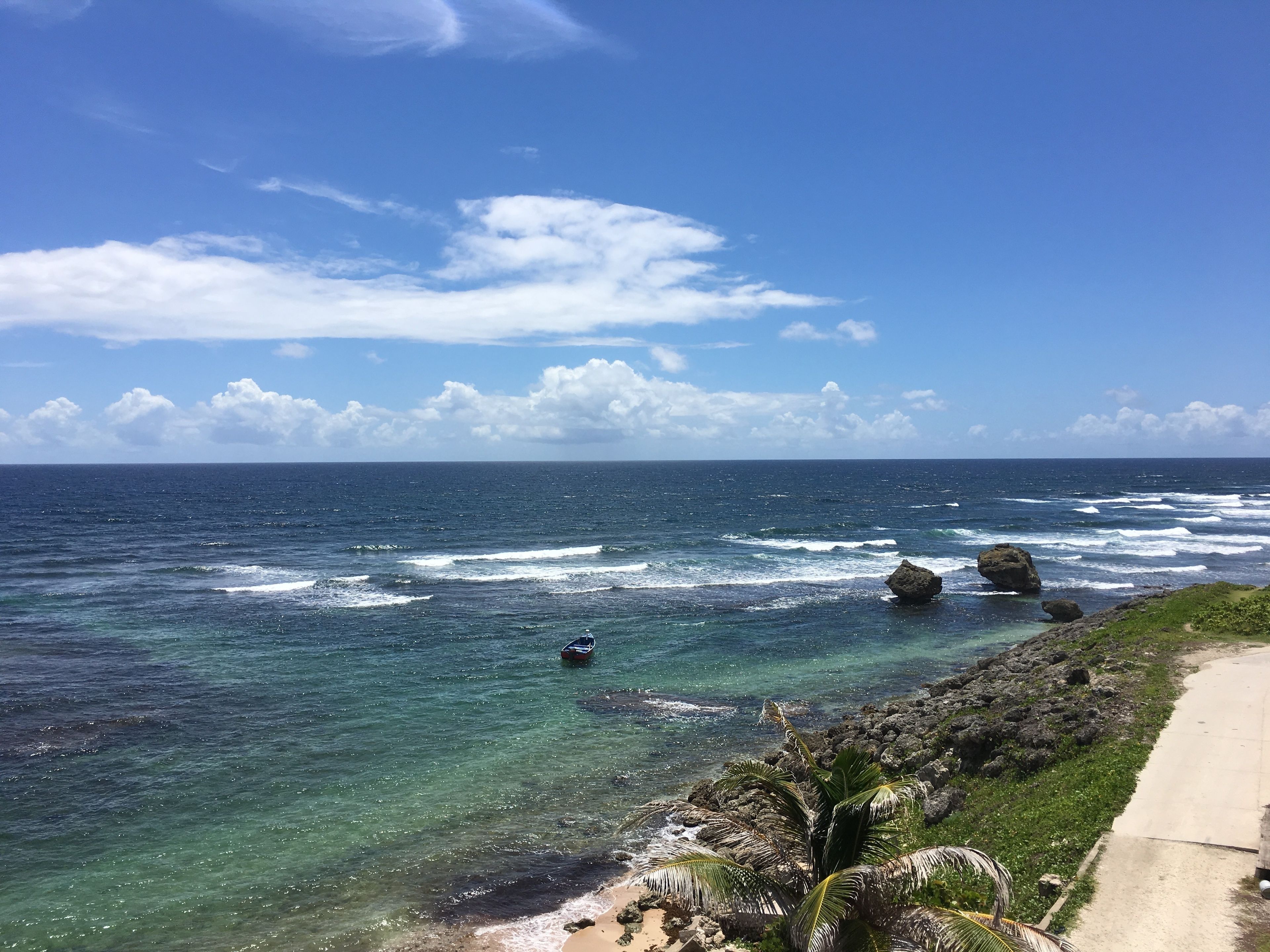 A coastal view with clear blue water, a sandy beach, and a concrete walkway.