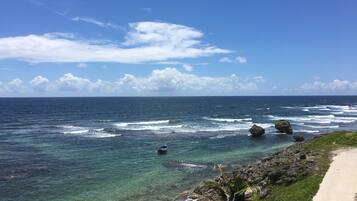 A coastal view with clear blue water, a sandy beach, and a concrete walkway.