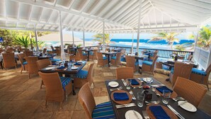 An outdoor dining area with wicker furniture, tables set for two, and a view of the ocean. - Atlantis Historic Inn (Bathsheba)
