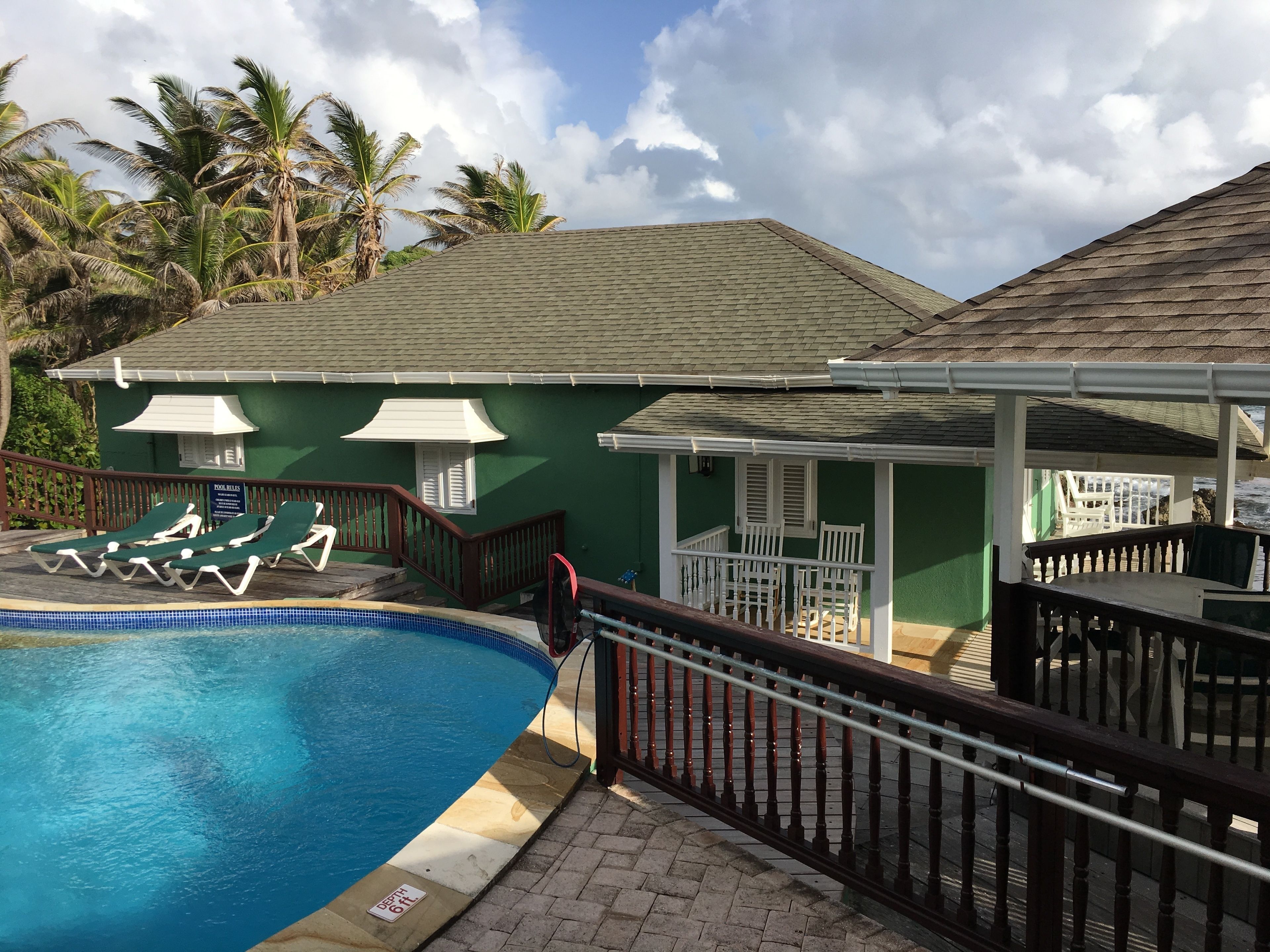 A pool area with lounge chairs, a covered seating area, and a building with a green exterior.