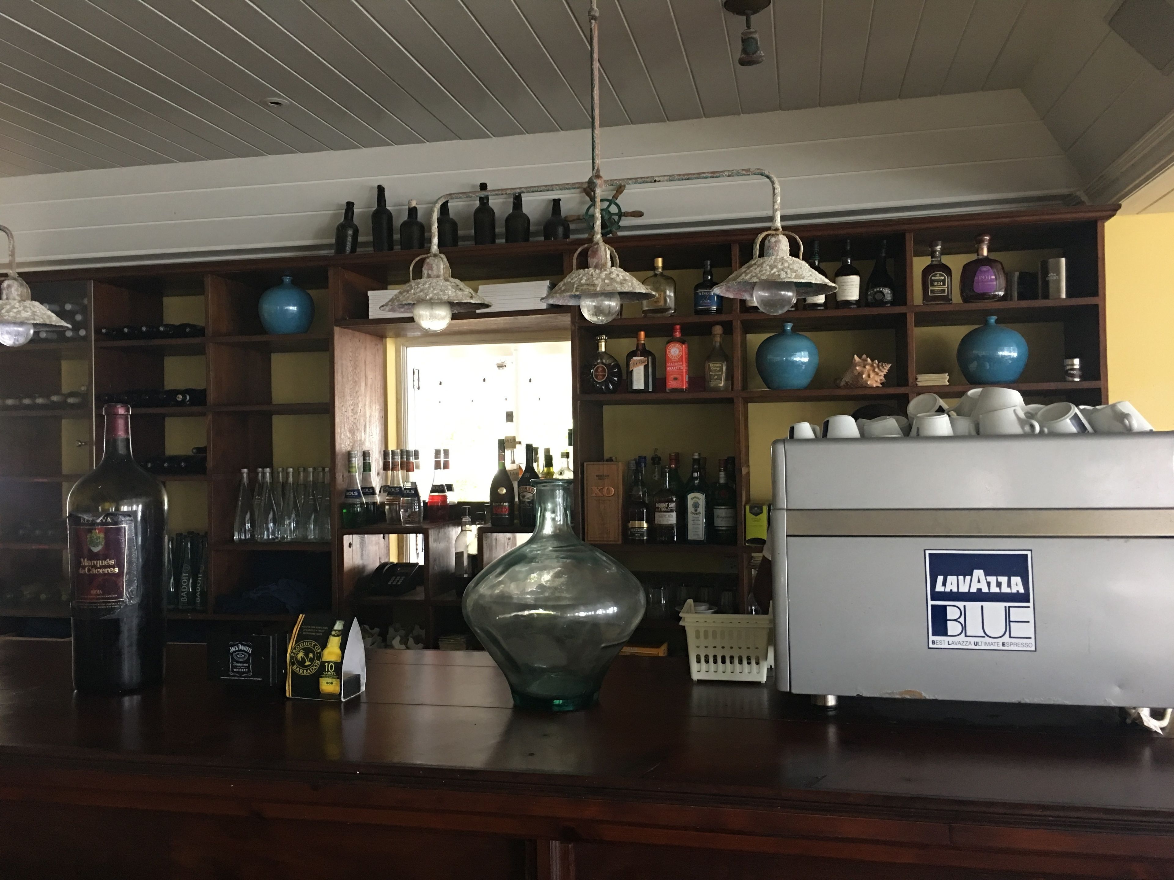 A bar area with shelves of liquor bottles, a large glass vase, and a coffee machine.