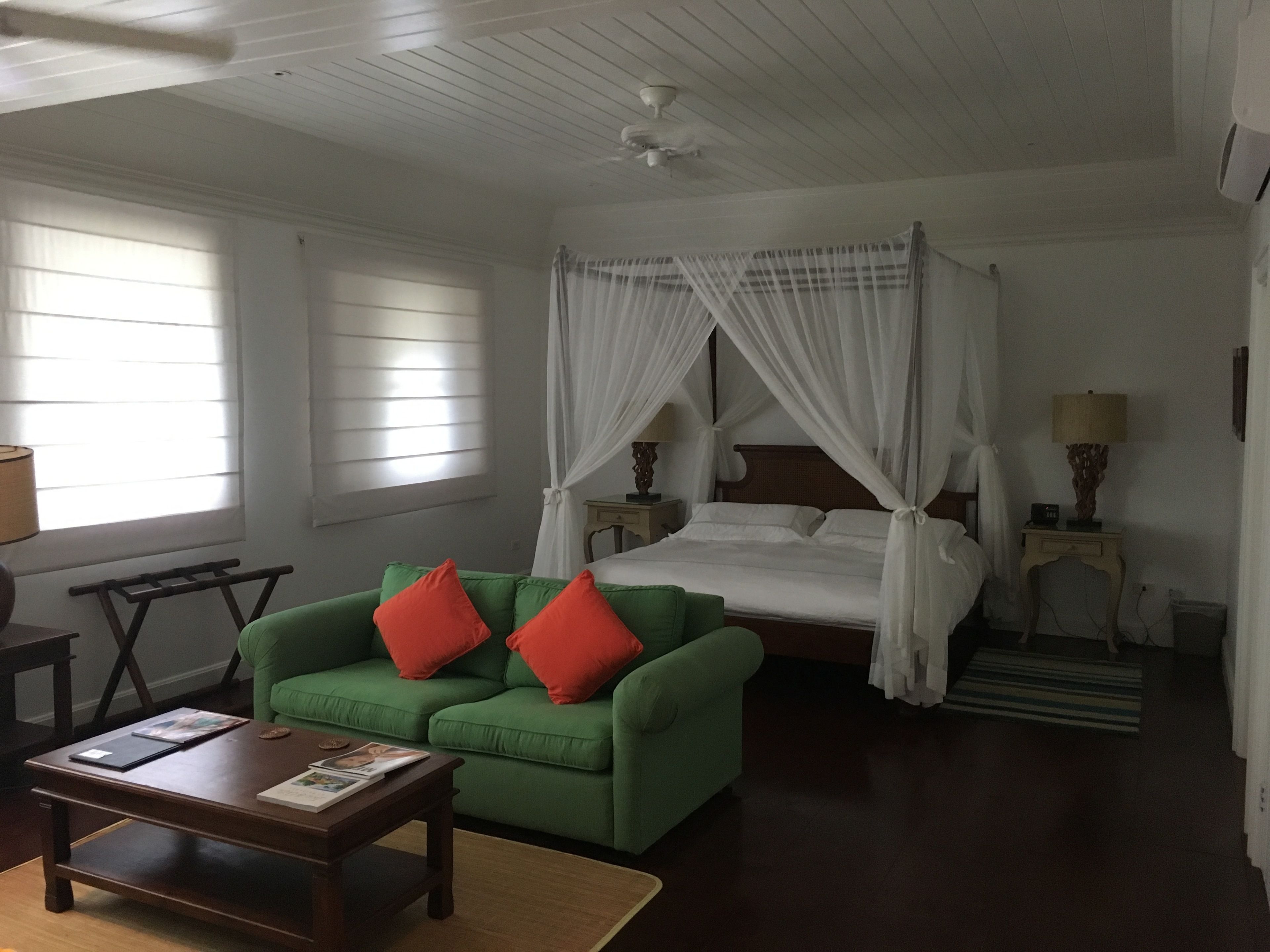 Una habitación con un sofá verde, una cama con dosel, una mesa de centro de madera y una mesita de noche con lámpara.