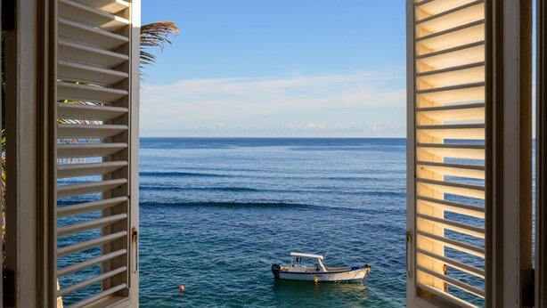 A view through open shutters of a calm sea with a boat in the distance. - Atlantis Historic Inn (Bathsheba)