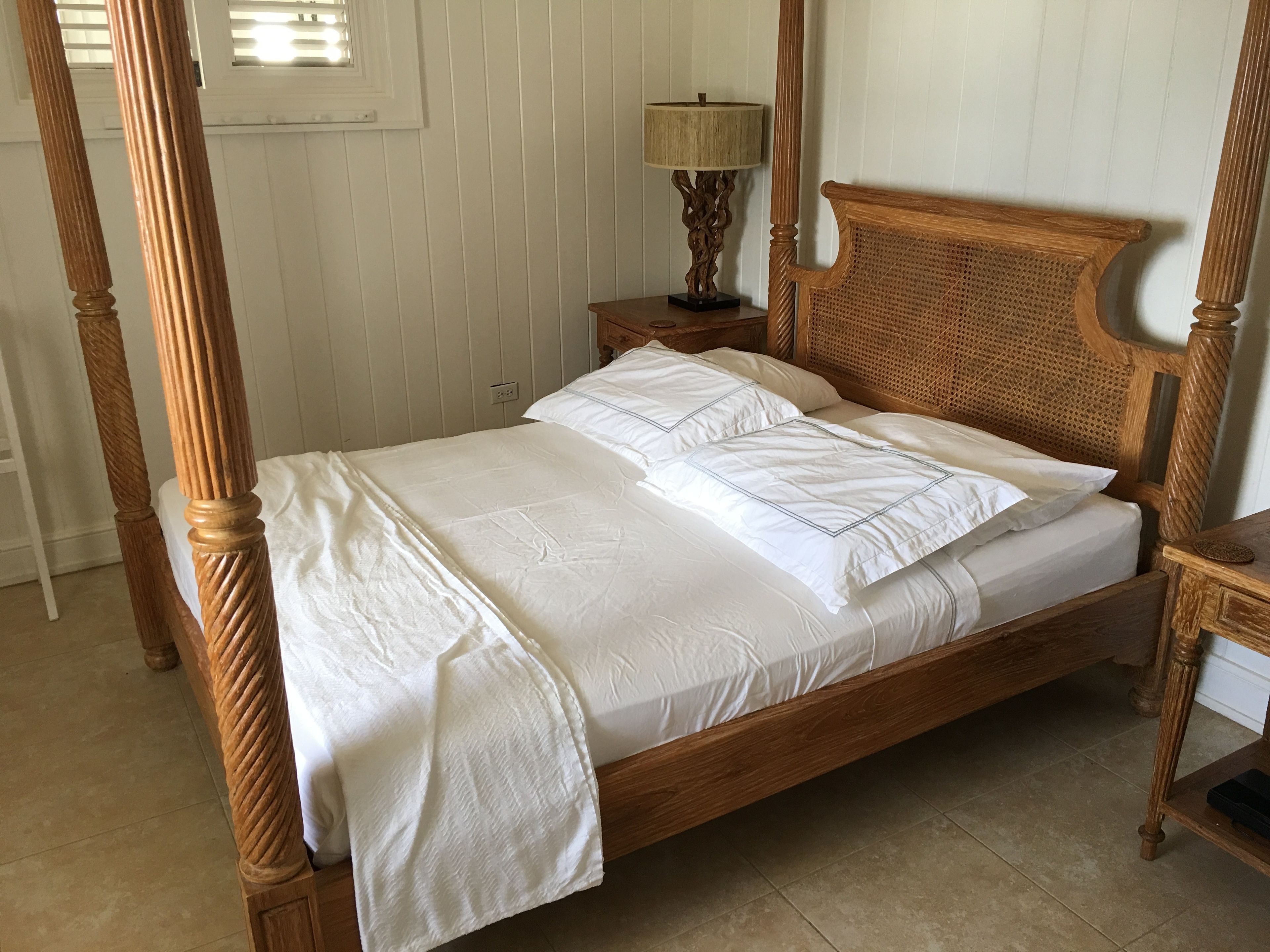 Uma cama de dossel com roupa de cama branca, cabeceira de madeira e mesa de cabeceira com abajur.