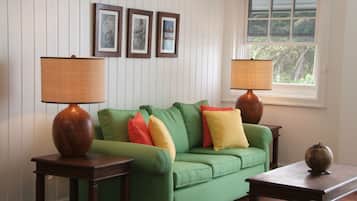 A green sofa with colorful cushions, two wooden tables with lamps, and framed artwork on the wall.