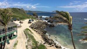 A coastal area with a beach, rocky shoreline, and a building with a green roof. - Atlantis Historic Inn (Bathsheba)