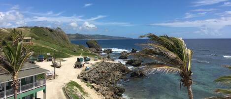 A coastal area with a beach, rocky shoreline, and a building with a green roof.