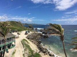 Zona costera con playa, costa rocosa y un edificio de techo verde.