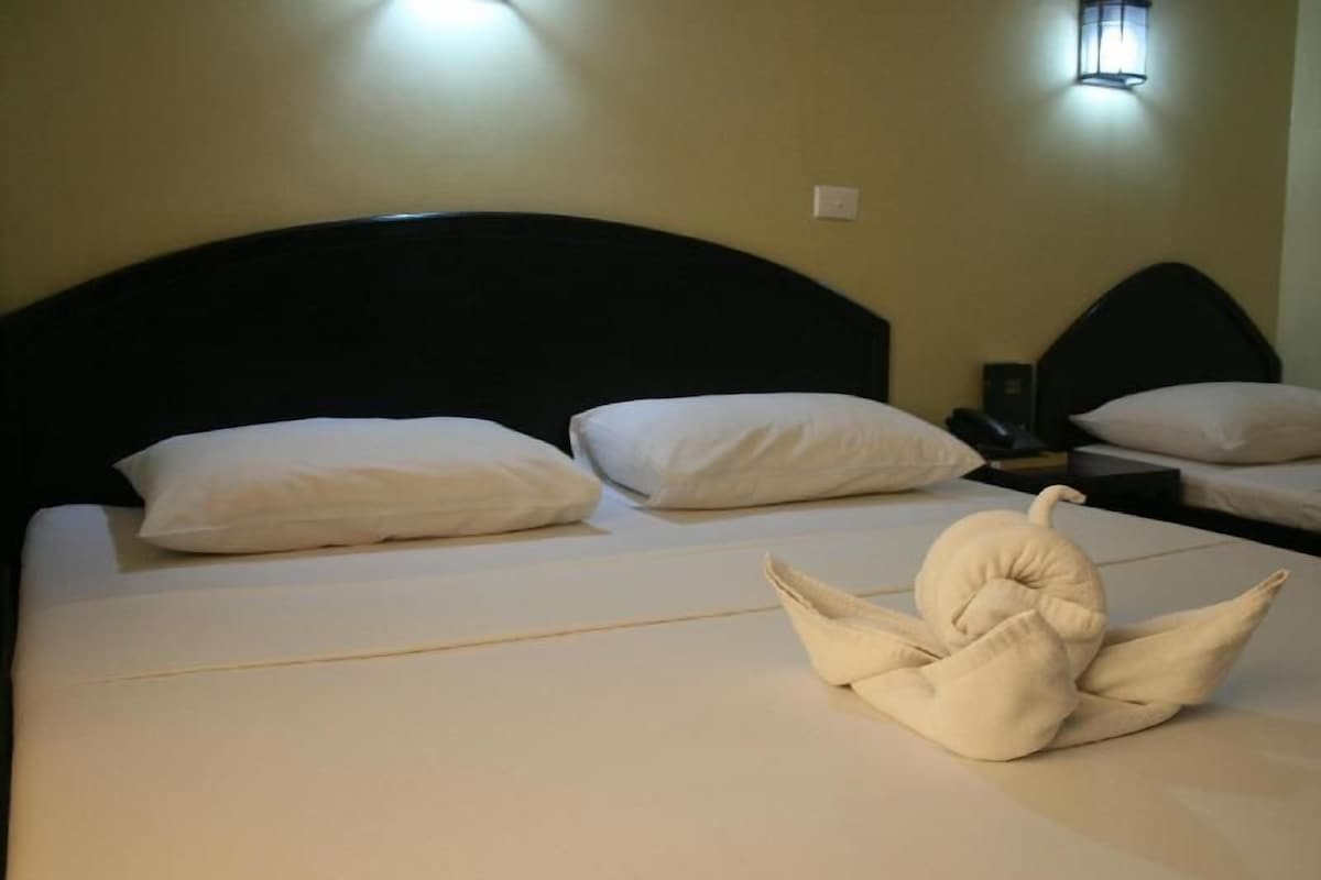 A hotel room with a neatly made bed, a bedside table with a lamp, and a wall-mounted light fixture.