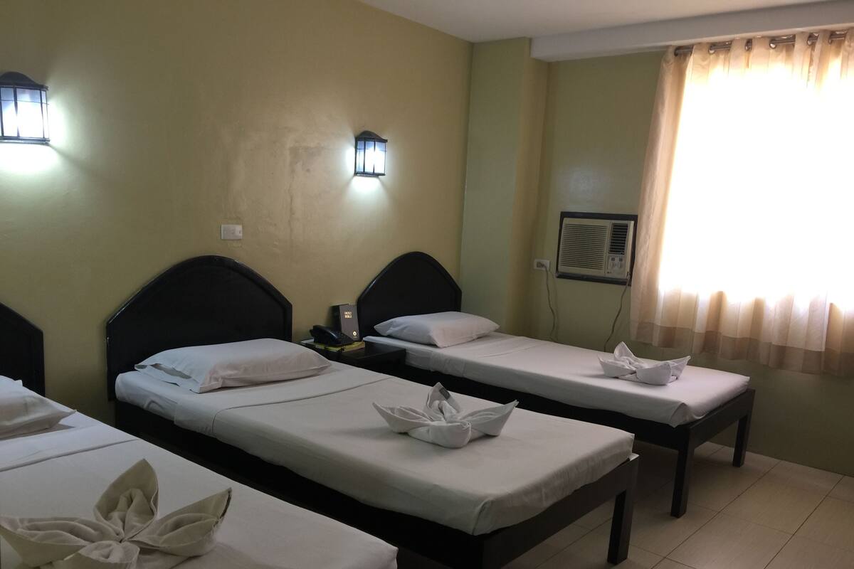 Ein Hotelzimmer mit zwei Einzelbetten, beide mit ordentlich bezogenen Bettdecken und Kissen. An jeder Seite der Betten befinden sich wandmontierte Leuchten.