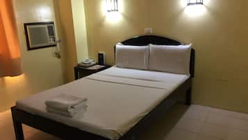 A neatly made bed with white linens, a bedside table with a phone and a book, and two wall-mounted lights.